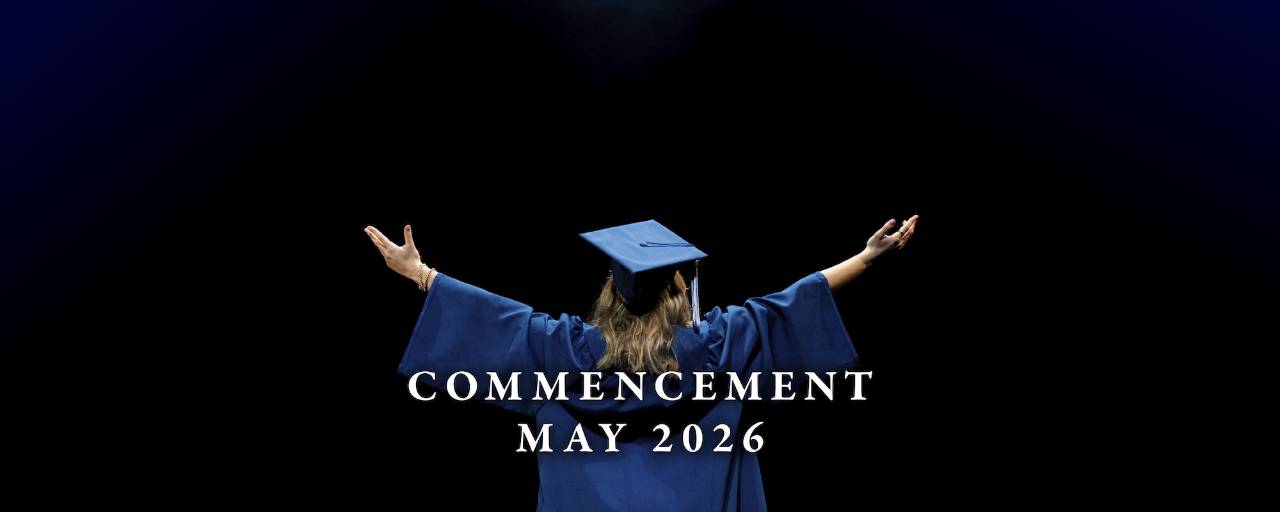 GVSU graduate, Ava Grillo, stands on a stage with arms stretched out